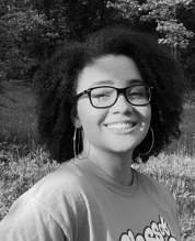 Black and white portrait of a young woman with dark corkscrew curls smiling in a meadow.