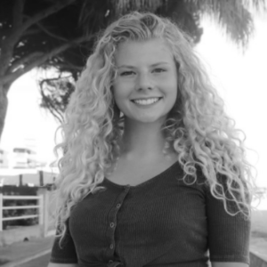 Black and white portrait of a young woman with long blond curls wearing a dark button-down shirt.